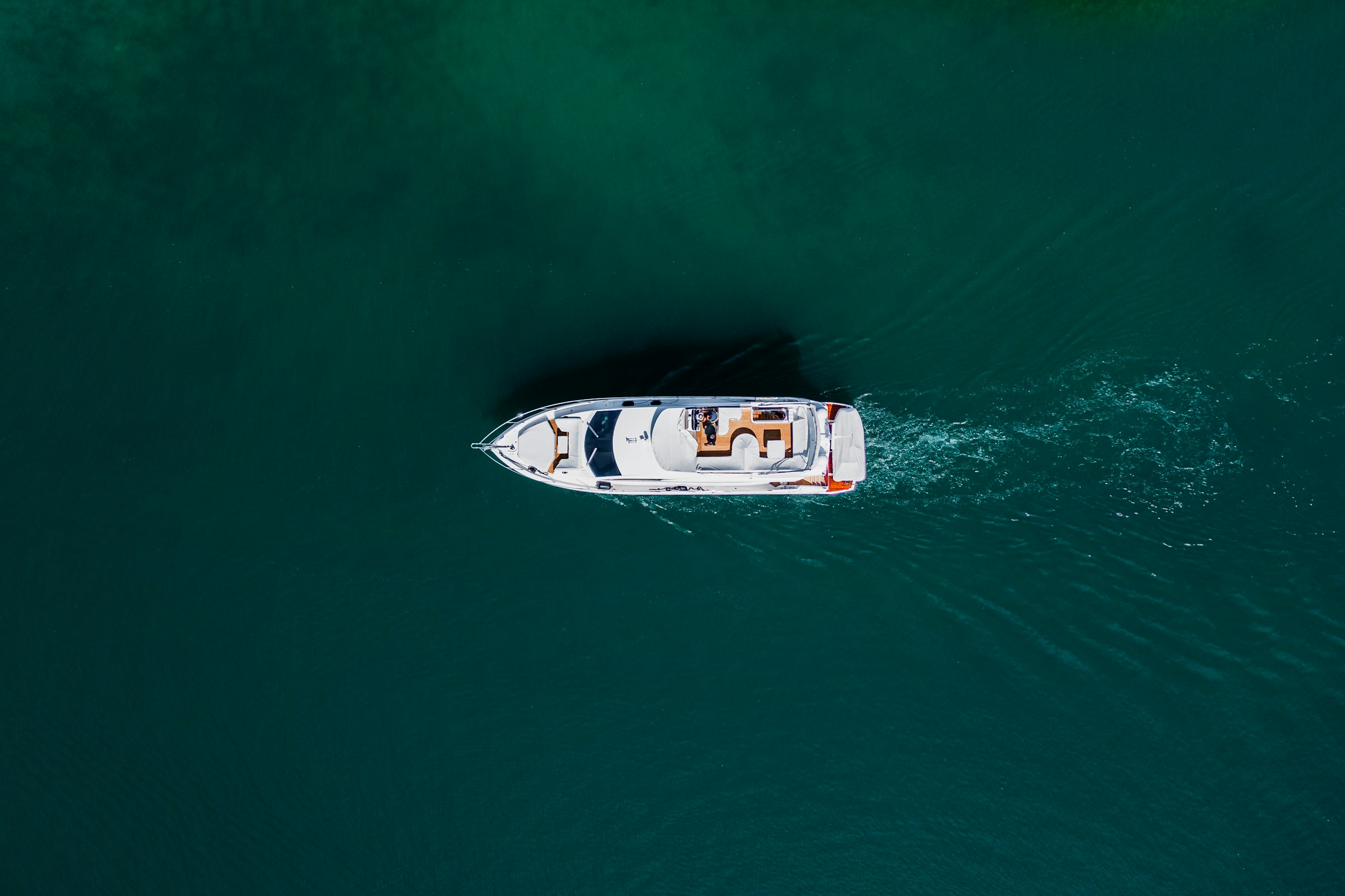 Motor yacht cruising on dark teal water, seen from above
